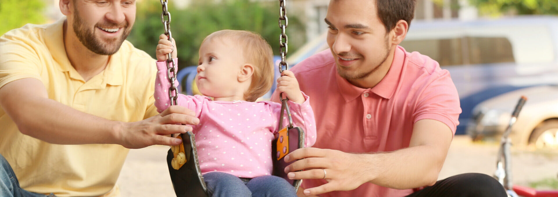 Male gay couple with adopted baby girl, outdoors