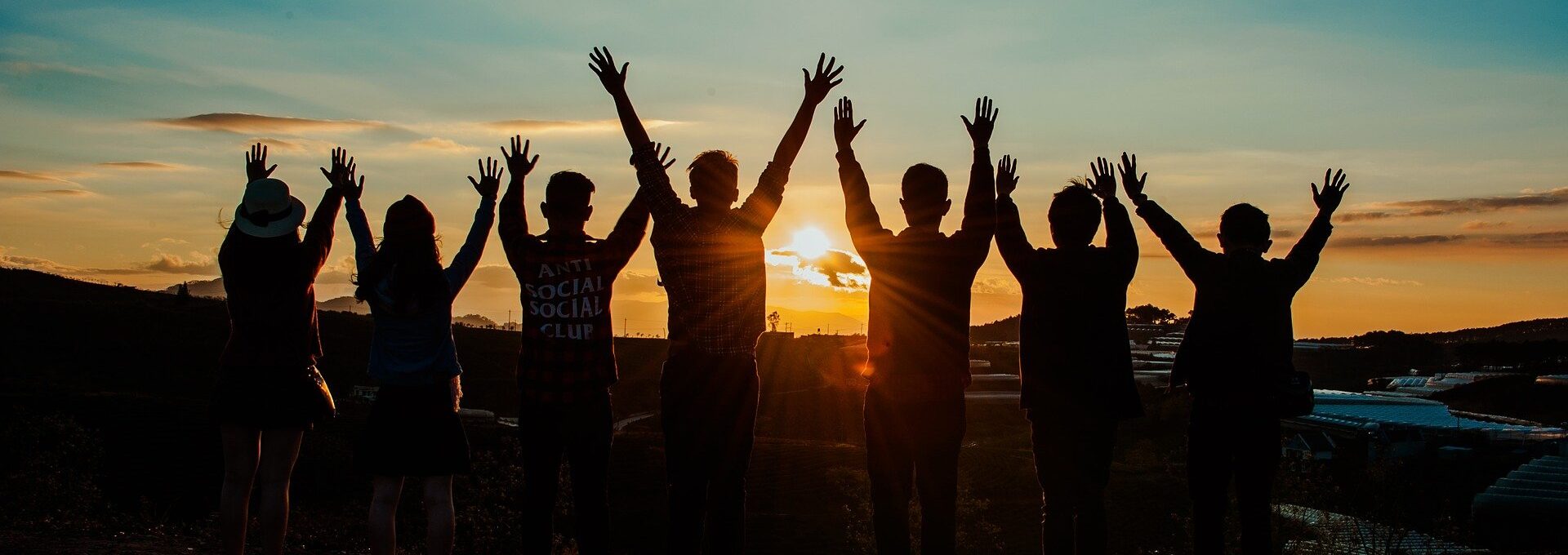 People om front of sunset with hands in the air