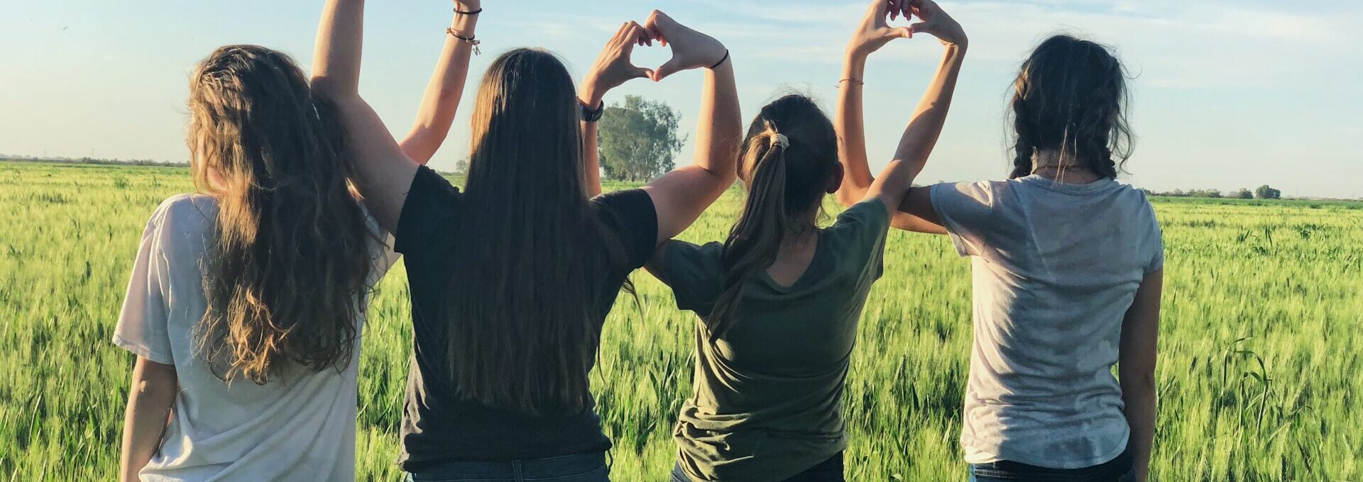 Girls in a field making heart shapes with their hands