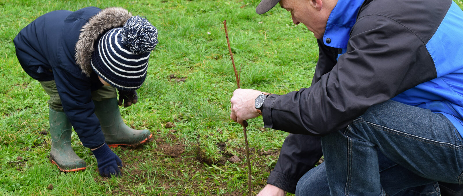 A young boy and man in hats and winter clothes plant a tree