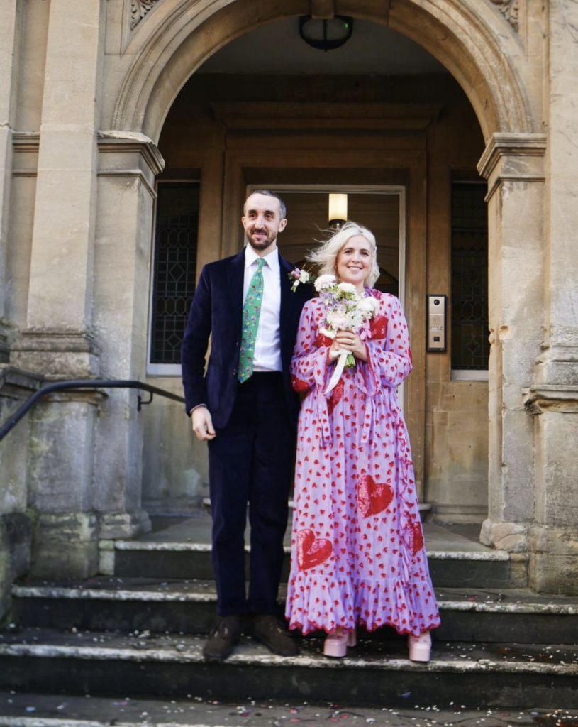 A man and woman holding flowers stand on Frome Town Hall steps after getting married