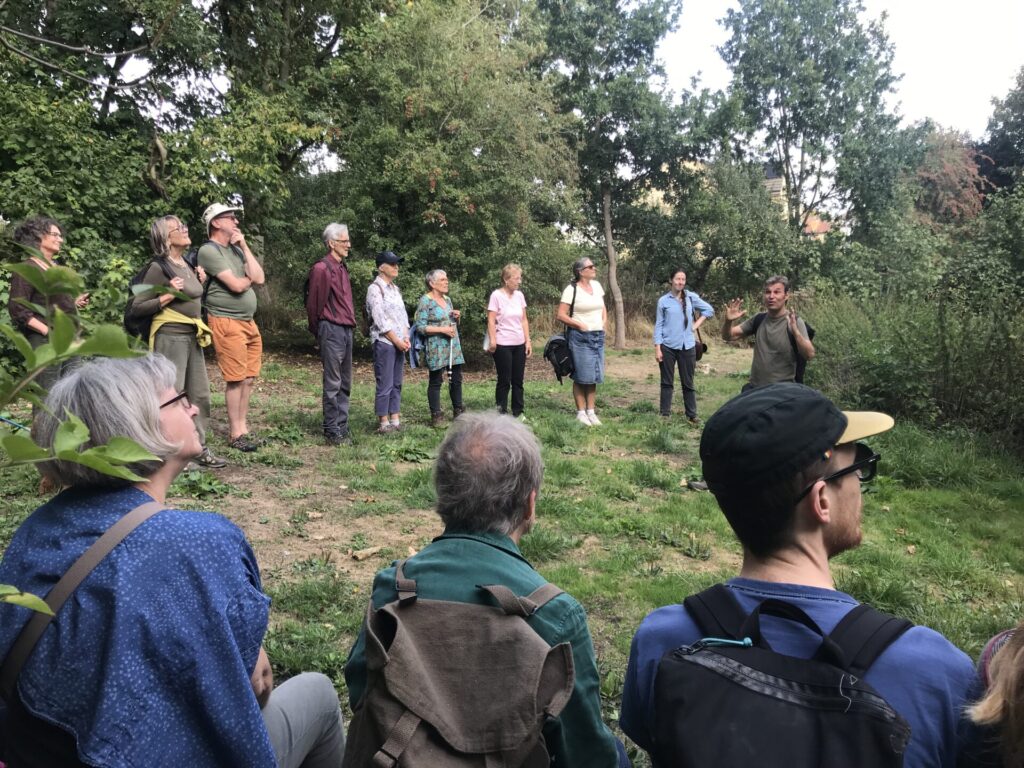 A group of people standing in a semi-circle listening to a tour guide, in the countryside. 