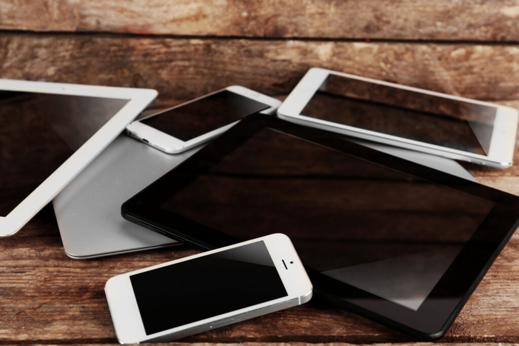 A pile of mobile phones and tablets on a wooden table