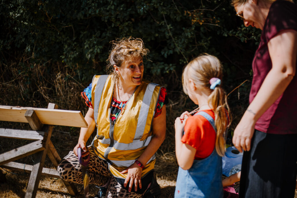 Ellen from local CIC Super Roots, smiling at a child and adult approaching her and a pile of scrap wood for making ramps