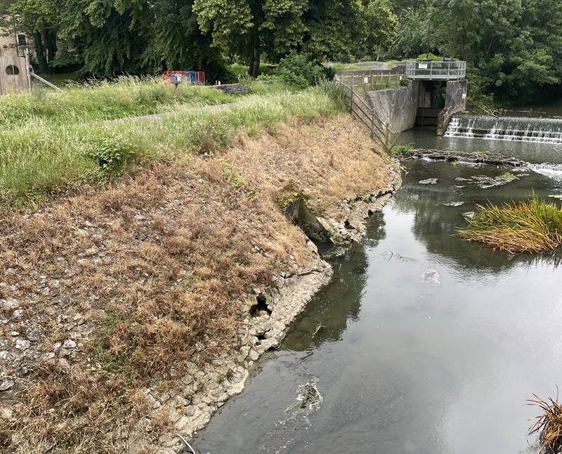 The view along the river at Welshmill, with the 'revetment' flood defence structure visible along the left hand side and the weir and sluice structure ahead.